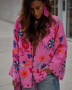 Détail d'un cardigan kimono rose vif avec broderies florales multicolores et texture en lin