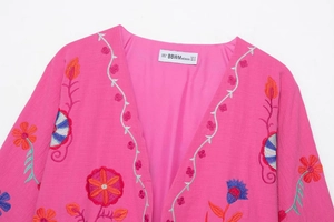 Détail de la broderie florale multicolore sur un gilet cardigan de couleur rose vif