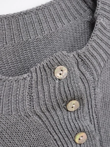 Détail d'un pull gris en maille col rond avec des boutons nacrés aux reflets irisés
