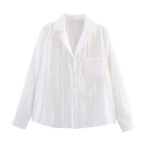 Detail shot of white long-sleeve shirt with embroidered pocket and textured fabric