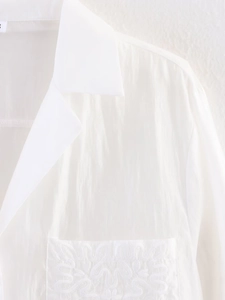 Detailed close-up of white textured shirt collar and pocket with fine embroidery