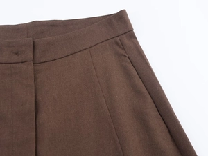 Detail of dark brown pleated trousers showing stitching and functional side pocket