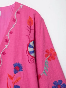 Détail d'un cardigan rose fushia avec broderies florales complexes et texture de tissu