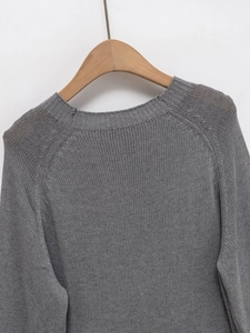 Détail du pull en maille grise à col rond montrant la texture fine et les manches raglan