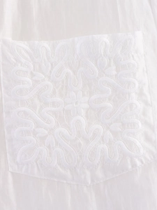 Close-up of intricate white floral embroidery on a pocket of a minimalist long sleeve shirt