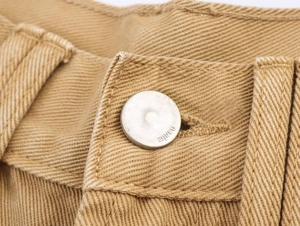 Macro shot of metal denim button and twill fabric texture on khaki straight-leg jeans