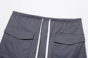 Detail of dark grey cargo pants featuring elastic drawstring waist and large flap pockets