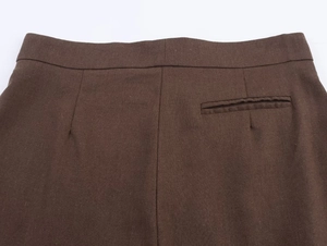 Detail of deep brown pleated pants featuring high-quality fabric texture and waist pocket