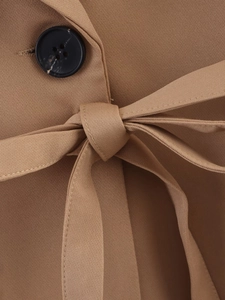 Detail of khaki trench coat featuring waist tie belt and black round button closure