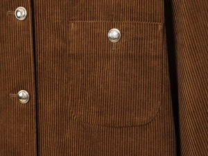 Macro detail of brown corduroy fabric texture with silver metal button and square pocket