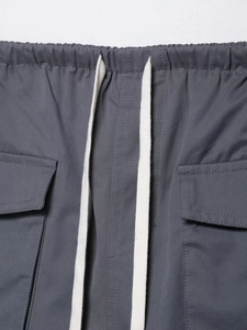 Detail of grey cargo pants showing elastic waistband with drawstrings and flap pockets