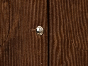 Close-up of brown corduroy fabric texture and polished silver metal button on a jacket