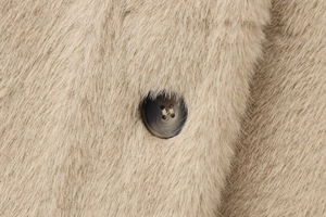 Détail macro de la texture fausse fourrure et bouton gris foncé sur manteau chameau