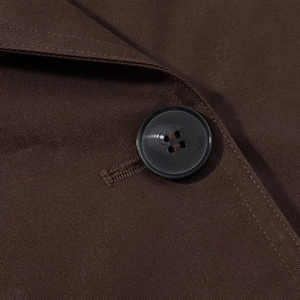 Detailed close-up of the dark brown twill fabric and button on short trench coat