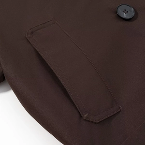 Close-up of deep brown trench coat featuring flap pocket with meticulous stitching and button