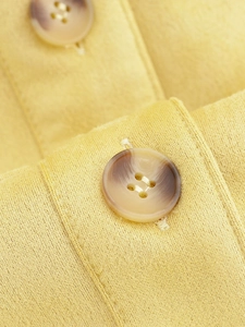 Macro detail of yellow faux suede fabric texture and tortoiseshell resin buttons on jacket