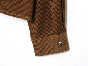 Macro detail of brown corduroy sleeve cuff with a silver-rimmed button and ribbed fabric texture