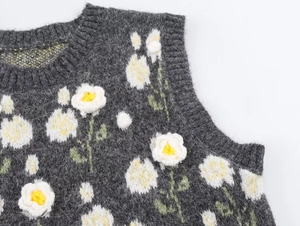 Close-up of 3D crochet daisy flowers on dark grey knitted vest with soft texture