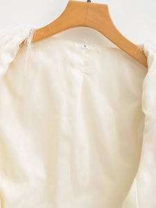 Detail view of cream fringe jacket featuring smooth satin lining and wooden hanger display
