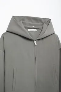 Detail view of a charcoal gray hooded jacket with zipper and brand label on white background
