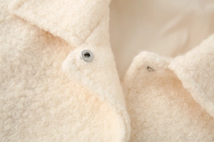 Detailed macro view of off-white faux shearling fabric with a silver snap button and lapel