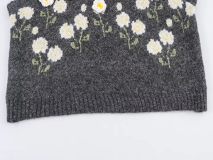 Detail of grey knit vest featuring 3D floral appliques and white daisy jacquard patterns