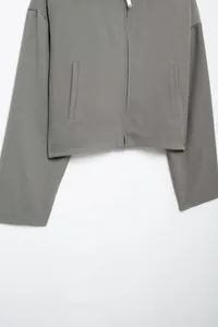 Detail of grey hooded jacket showing silver zipper, vertical pockets and twill fabric