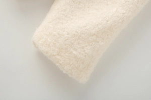 Detailed close-up of cream faux shearling fabric with soft curly texture and warm finish