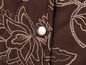 Detail of dark brown quilted jacket featuring light floral stitching and silver metal snap button