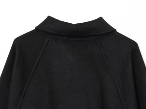 Detail shot of black wool blend coat neckline and raglan sleeve stitching on white background