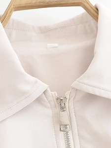 Macro detail of beige jacket neckline showing lapel collar and metal zipper quality