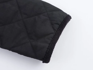 Detail of black quilted jacket featuring diamond stitching and corduroy piped edges