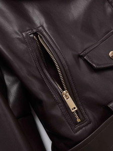 Détail de la veste en cuir marron foncé avec fermeture éclair dorée et bouton métallique