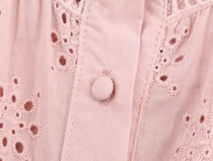 Close-up of pink long-sleeve shirt featuring intricate eyelet embroidery and matching button