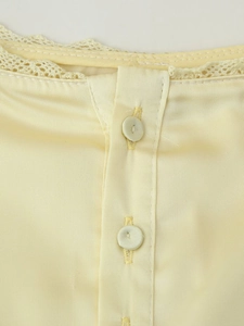Détail du haut en satin jaune pâle avec dentelle délicate et boutons en tissu assortis