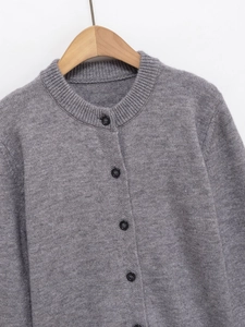 Close-up of grey knit cardigan showing crew neck and black contrast buttons on wooden hanger