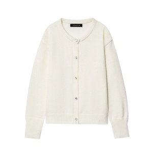 Detail of round neck knit cardigan with pearl buttons and ribbed cuffs on cream fabric