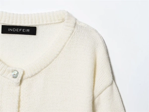 Detail of round neckline and pearl button on soft white knit cardigan fabric texture