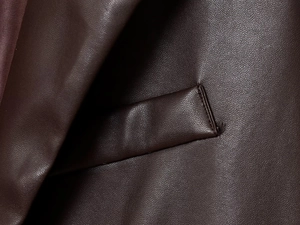 Détail macro de la texture du cuir marron foncé et des coutures d'une poche de blazer