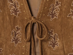 Detail of khaki suede vest neckline with dark brown floral embroidery and tie closure