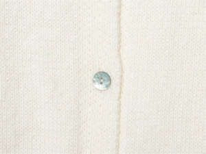 Close-up of white knit sweater featuring a premium iridescent mother-of-pearl button