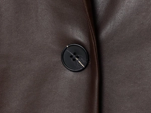 Détail macro de la texture du similicuir et du bouton noir sur le blazer marron