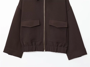 Detail of dark brown jacket with metal zipper, large flap pockets, and elastic hemline