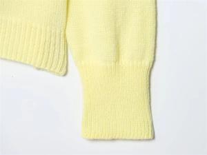 Close-up detail of light yellow knit sweater showing ribbed cuffs and soft fabric texture