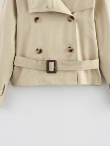 Détail d'un trench-coat court beige à double boutonnage avec boutons ambre et ceinture à boucle