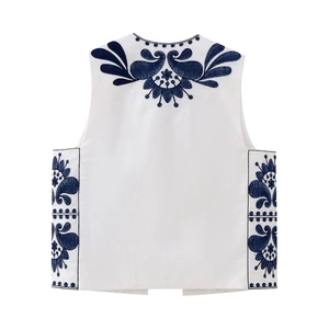 Close-up of ethnic embroidery with blue floral and paisley patterns on white vest
