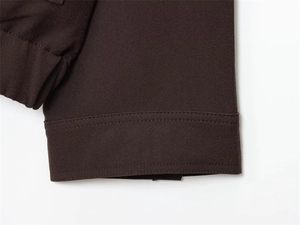 Detailed close-up of dark brown woven fabric jacket sleeve with neat stitching finish