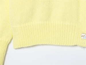 Close-up of soft yellow knit sweater with ribbed hem and elegant pearl button detail