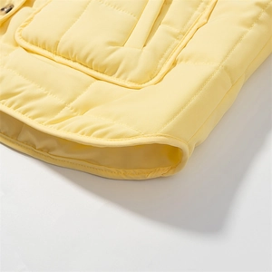 Detail of light yellow quilted jacket showing precision stitching and hem border finishing