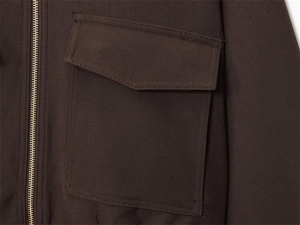 Macro detail of dark coffee jacket featuring metal zipper and pointed flap pocket